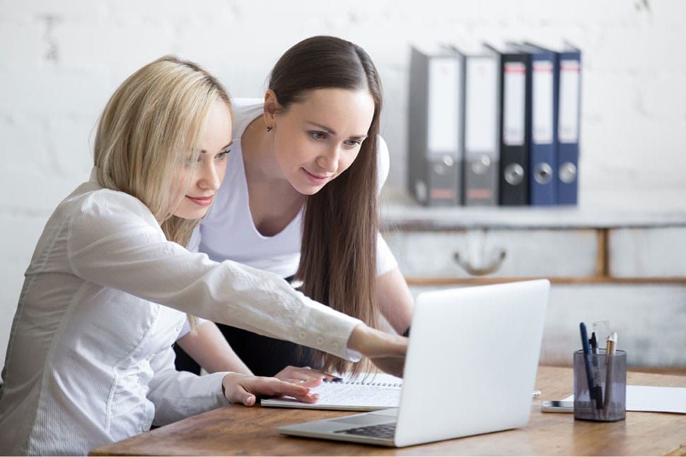 Zwei Frauen vor einem Laptop, AdWords Trainerin zeigt auf Laptop