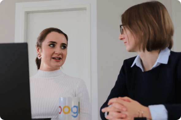Zwei Frauen sprechen miteinander, Laptop und Google Tasse auf dem Tisch